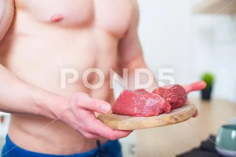 Muscular Man With A Naked Torso In The Kitchen With A Piece Of Beef