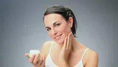 Female beauty, beautiful young woman putting lotion and cream on face
