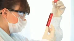 Female scientist examines test tube with red liquid, steadicam shot
