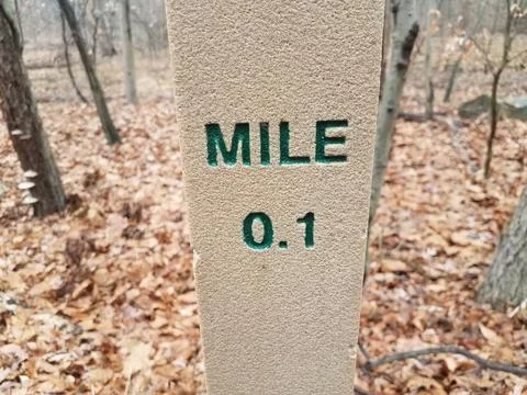0.1 mile marker post in forest or woods with leaves Stock Photos