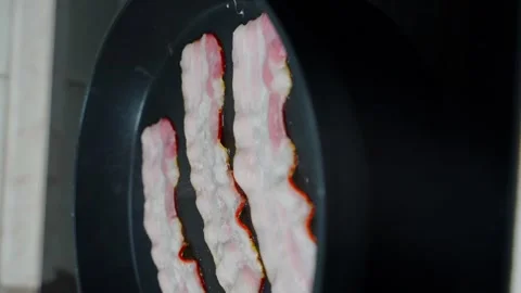 01 Three strips of bacon are fried in a pan in slow motion vertical Stock Footage 221127234