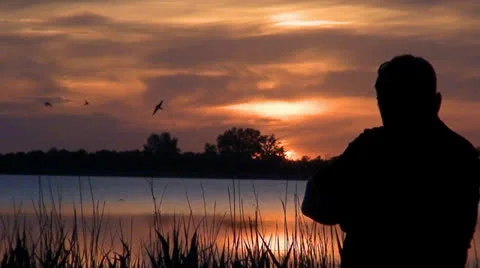 010 A man stands on a background sunset at a lake Stock Footage 25144232