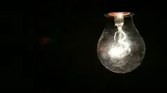 Old lightbulb swinging on black background
