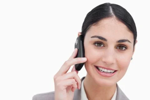 Close up of smiling businesswoman talking on cellphone against a white background xkwx 20s,Young Adult,Woman,Caucasian,Beautiful,Businesswoman,Career,Confident,Elegant,Employee,Happy,Pretty,Smile,Standing,Full Suit,Worker,Smiling,Well Dressed,Brown Hair,Tied Hair,Brunette,Mobile,Phone,Talking,Calling,Listening
