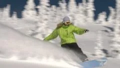 Snowboarder carves through beautiful powder on bright sunny day.