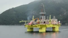 Oil rig located in sea near coastline with forest on mountain