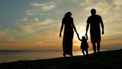 Happy family walking on sea coast. Silhouettes sunset.