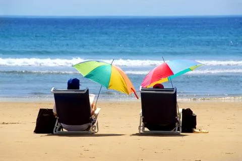 a  couple  relaxing  on  a  beach  under  colorful  umbrellas xkwx couple,  people,  romantic,  person,  love,  two,  pair,  chair,  chairs,  beach,  beaches,  sand,  sandy,  water,  sea,  ocean,  seashore,  shore,  coast,  coastline,  outside,  outdoor,  outdoors,  summer,  vacation,  vacations,  holiday,  holidays,  weekend,  sit,  sitting,  relax,  relaxing,  umbrella,  umbrellas,  colorful,  color,  read,  reading,  view,  back,  happy,  tropics,  tropical,  island,  maine,  yellow,  blue,  getaway,  folding