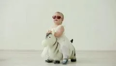 Funny little girl in white dress and red sunglasses jumps on Zebra