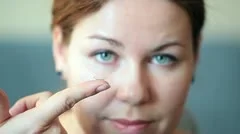Young woman inserting clear contact lens in her eye