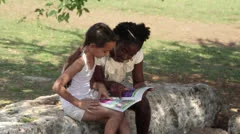 Young people and education, two little girls reading book in city park