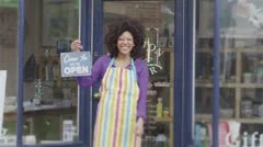 Happy female shopkeeper holds up a sign to show she is open for business
