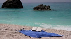 Summer relax - book, sunglasses at sea towel near the blue water