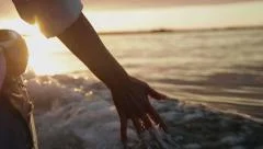 Hand glides over waves at sunset
