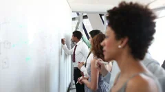 Business people brainstorming ideas on a whiteboard in a large corporate office.