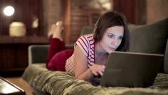 Beautiful woman with modern laptop lying on sofa at home HD