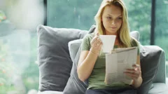 Attractive young woman relaxing at home with newspaper and cup of coffee