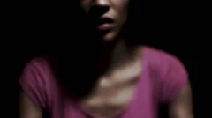 Woman praying with hands clasped together on dark background.