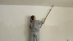 woman painting an interier wall with a paint roller with an extended handle
