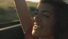 Happy Hispanic Teen Girl Rides In The Back Of Convertible, Raises Arm in The Air