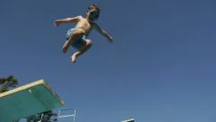 Boy jumping from springboard and diving in Swimming Pool. Kids. Slow Motion