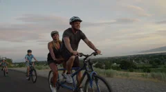 Tracking medium shot of family bike riding on road at sunset / Cedar Hills,