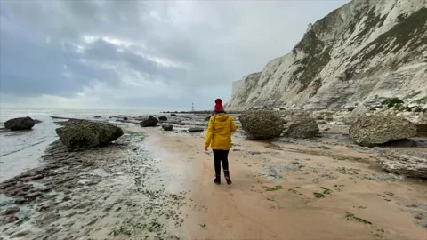 035 Lady walking on beach in yellow coat after storm on golden sand with whit Stock Footage