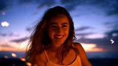 Smiling young woman with sparkler at sunset in slow motion