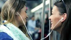 Happy girlfriends listen to music and sing while riding metro train HD