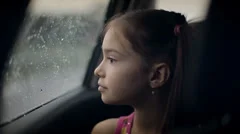 Little girl looking out from car window. Rainy weather