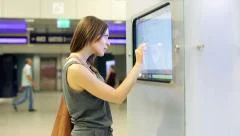 Woman checking trains timetable at modern touchscreen info kiosk HD