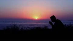 man praying by the sea at sunset