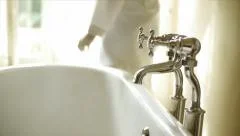 Woman turning off hot water bathtub faucet in the bathroom