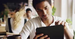Mixed race man using digital display touchscreen tablet ipad device in cafe