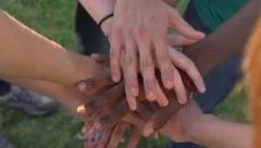 Hands of all colours and races stack together - slow motion.