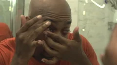 A black man, in reflection, inserts a contact lens