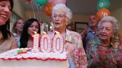 Family celebrates birthday party for a 100 year old lady with cake and candles