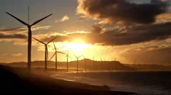 Wind turbine power generators silhouettes at stormy ocean coastline at sunset
