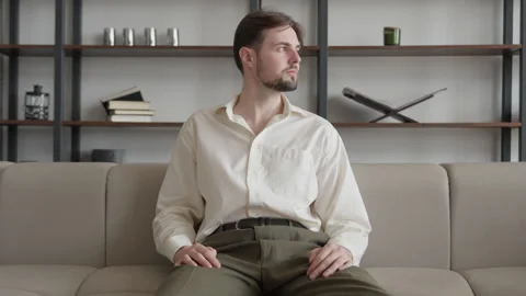 0481 Thoughtful Man Sitting On Sofa In Modern Minimalist Living Room Interior Видео 318930036