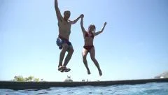 Young Happy Couple Holding Hands Running And Jumping Into Swimming Pool