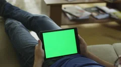 Man is Laying on Couch at Home and Watch on Tablet with Green Screen