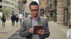 Young African Asian man in city walking using tablet pc computer