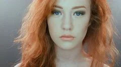 Beautiful teenage girl with red blowing hair and blue eyes on grey studio