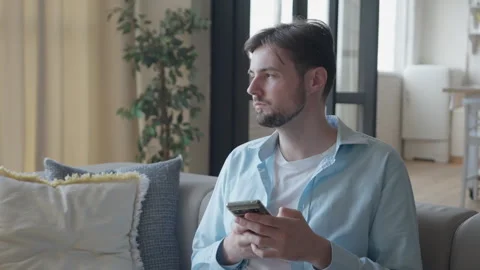 0504 Man Checking Phone And Thinking While Sitting On Modern Cozy Living Room Stock Footage 318930588