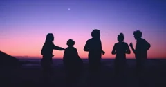 Group of friends dancing on the beach at dusk