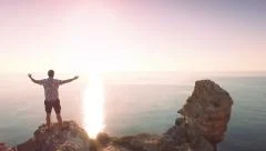 Man Raising Hands In Worship Pose At Top Of Ocean Cliff Rocks Sunrise Religious