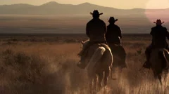 Slow motion dusk shot of cowboys riding towards mountains.