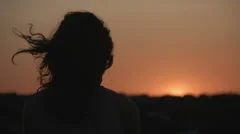 Dark silhouette of woman watching sunset, sunrise. Hair waving in wind. Mystery