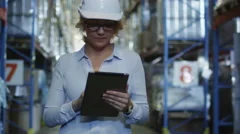Woman Manager in Hard Hat Walking in Logistic Warehouse. Holding Tablet PC