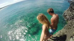 Young Fit Travel Couple Holding Hands and Jumping off Cliff into Blue Sparkli